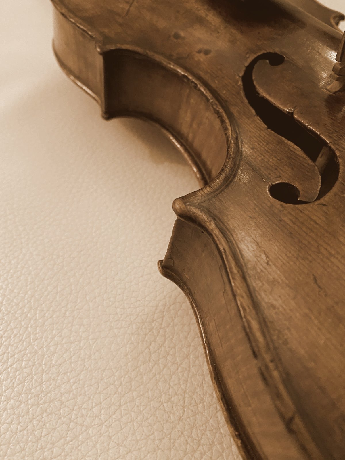 Alte Geige auf hellem Leder, Detail mit F-Loch, in warmem Sepia